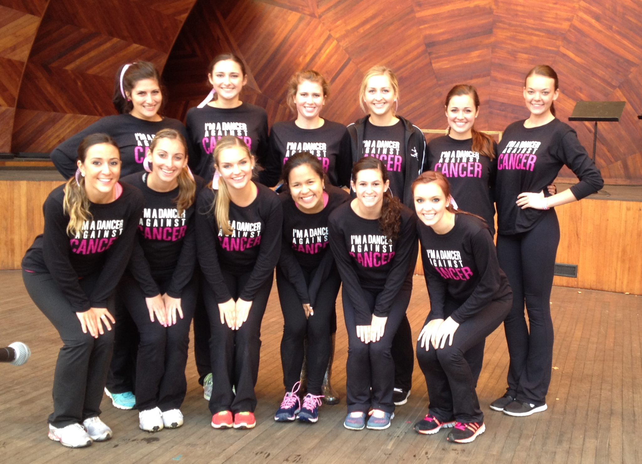 A group of dancers poses on stage wearing matching custom t-shirts that say, "I'm a dancer against cancer." 