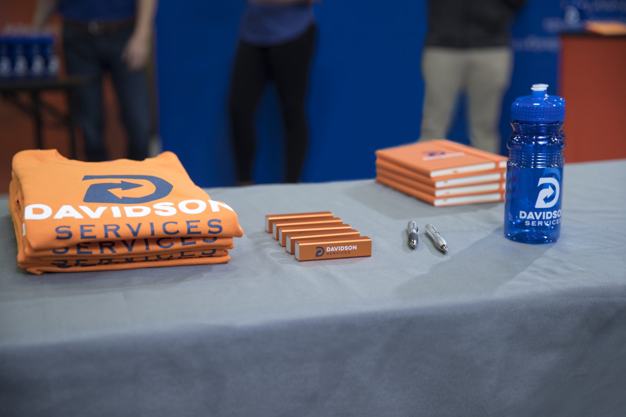 t-shirt, notebooks, pens, and water bottles are displayed at a tradeshow
