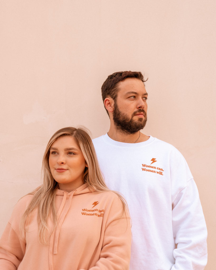 Becca and a male friend showing off the "Women Can. Women Will." logo on their custom apparel.