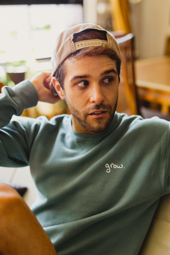 Tyler showing off his custom merch: the text "grow." printed on a Hanes Comfort Garment Dyed Crewneck Sweatshirt