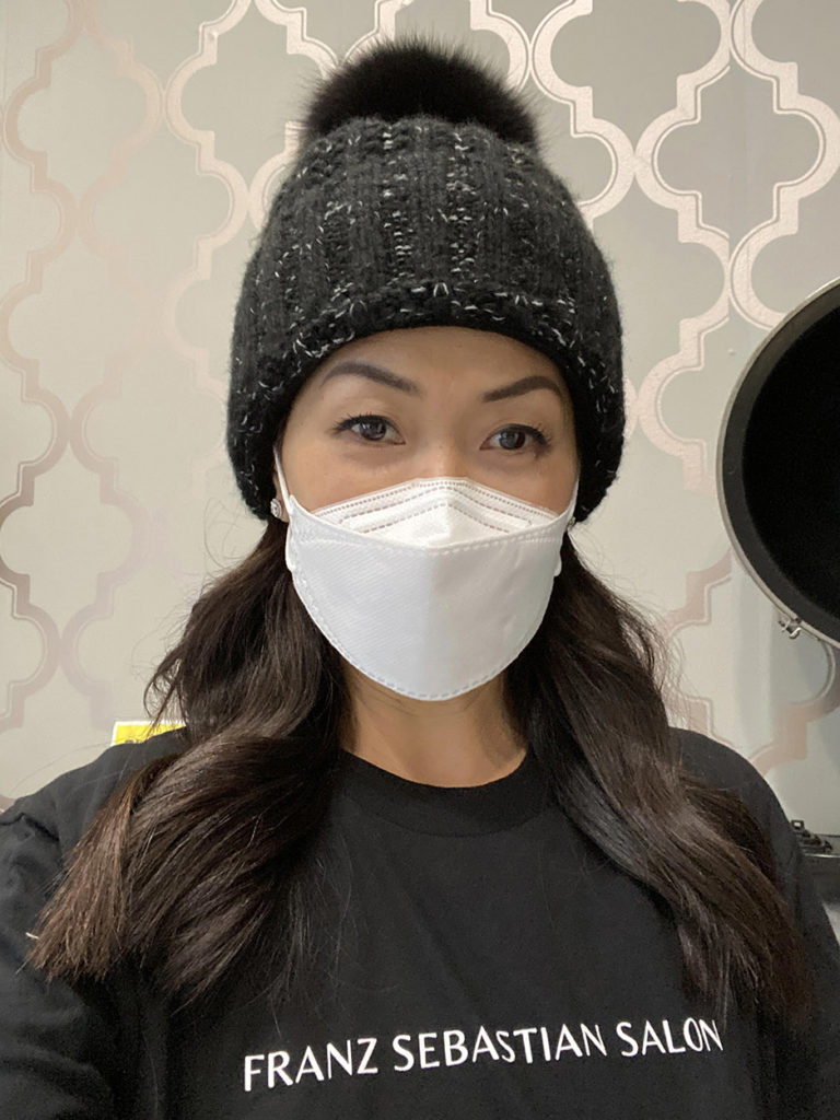 Stylish woman in a mask and hat wearing a black shirt with the text Franz Sebastian Salon