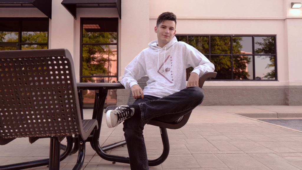 Young man sitting at a table outside wearing a custom hoodie