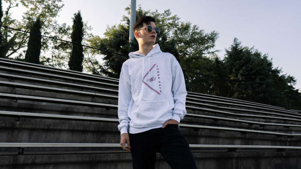 Young man with sunglasses wearing custom hoodie in front of bleachers