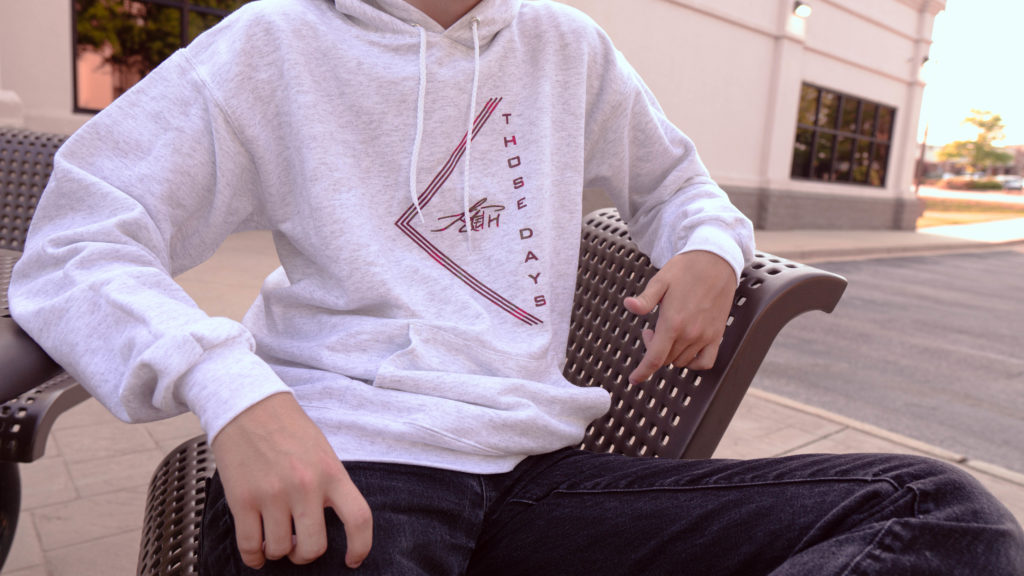 Close up of ash-colored hoodie with red text saying "Those Days" and a signature