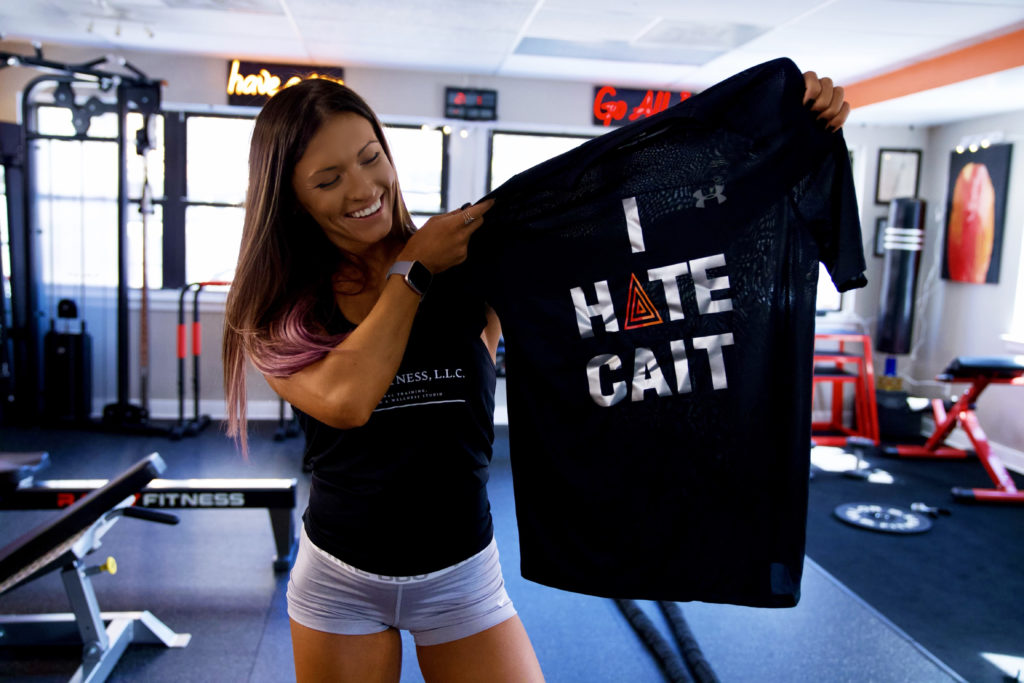 Woman in gym showing off a shirt with I HATE CAIT printed on it