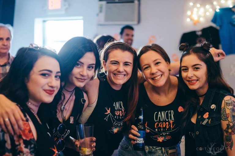 Five women smile at the camera with their arms around each other. You can see two of their shirts which both say Cancer Can't Kill Love.