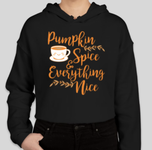 A black cropped hoodie with orange text that reads "Pumpkin spice and everything nice." On the left, there is a very cute white and orange mug with a smiley face.