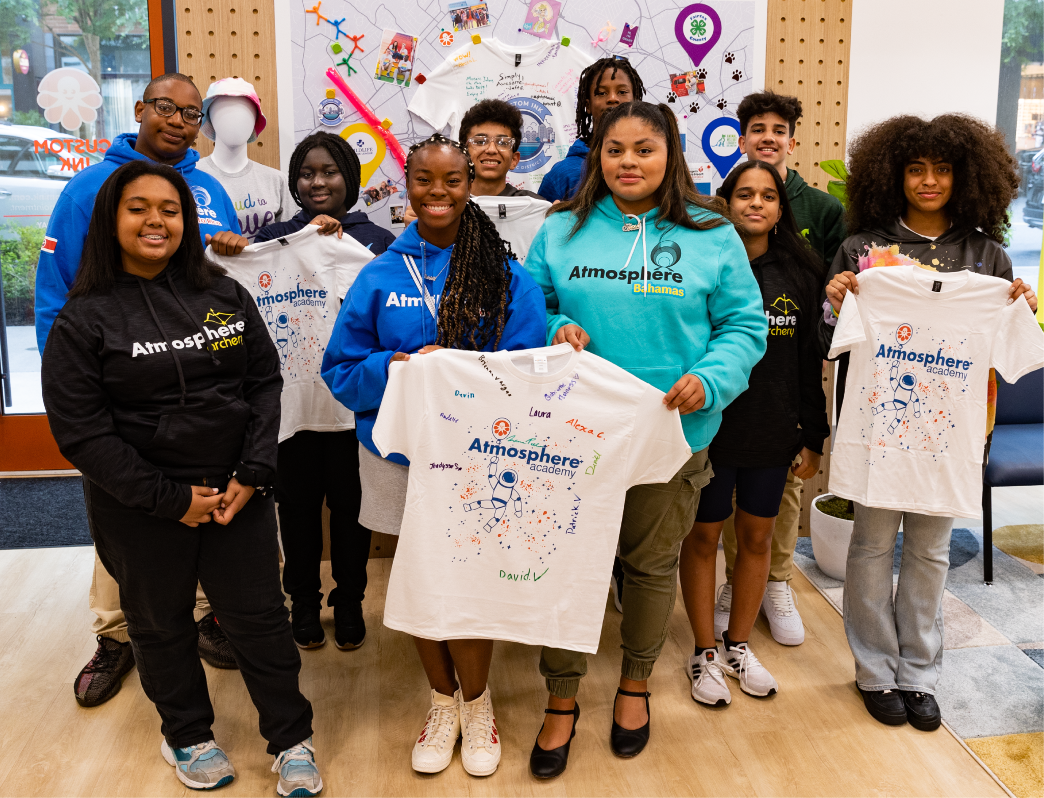 A group of students stand in a classroom, wearing shirts featuring the logo for Atmosphere Academy and an astronaut design.