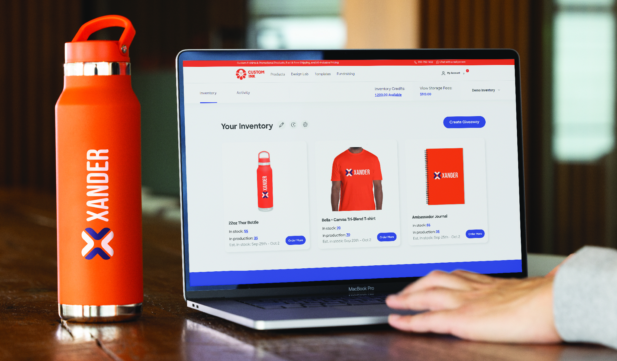 A custom water bottle next to a computer screen shows an online dashboard for Custom Ink's Inventory and Distribution platform with other custom products featuring the same logo.
